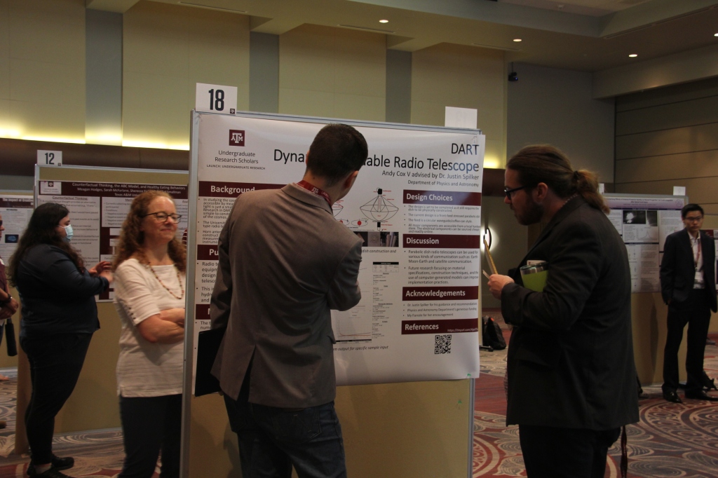 Student points to their research poster as a professor looks on. 